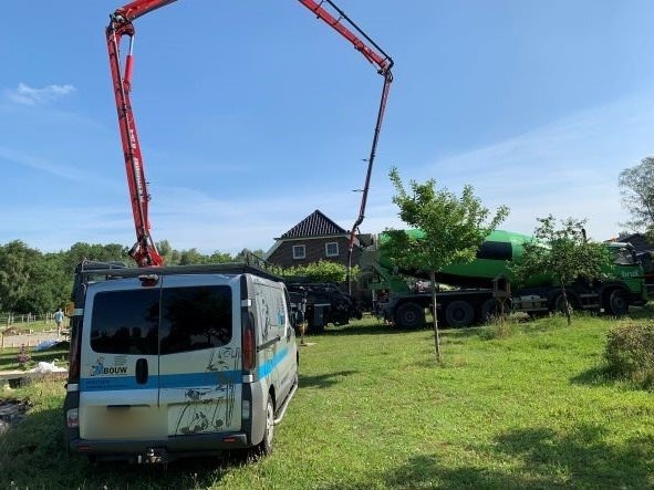 De bus van MBouw op een bouwplaats, met een betonpomp op de achtergrond