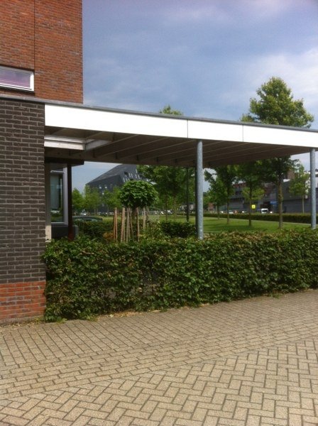 Carport met wit dakrand en stalen kolommen naast een rijtjeswoning